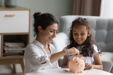 Happy,excited,indian,mother,and,kid,dropping,cash,into,piggybank.