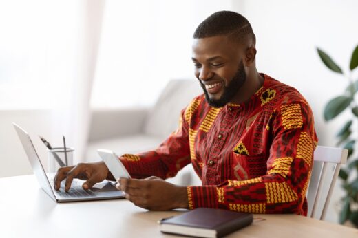 Cheerful,black,man,in,traditional,african,clothes,using,smartphone,and