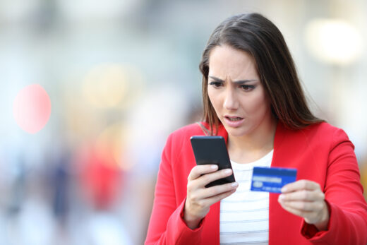 Worried,woman,holding,credit,card,looking,at,smart,phone,in