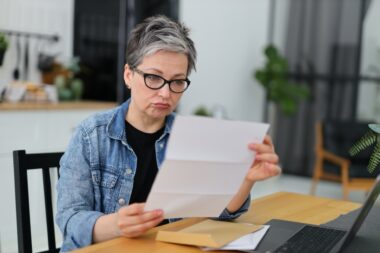 Upset,senior,woman,reading,mail,or,bill,at,table.