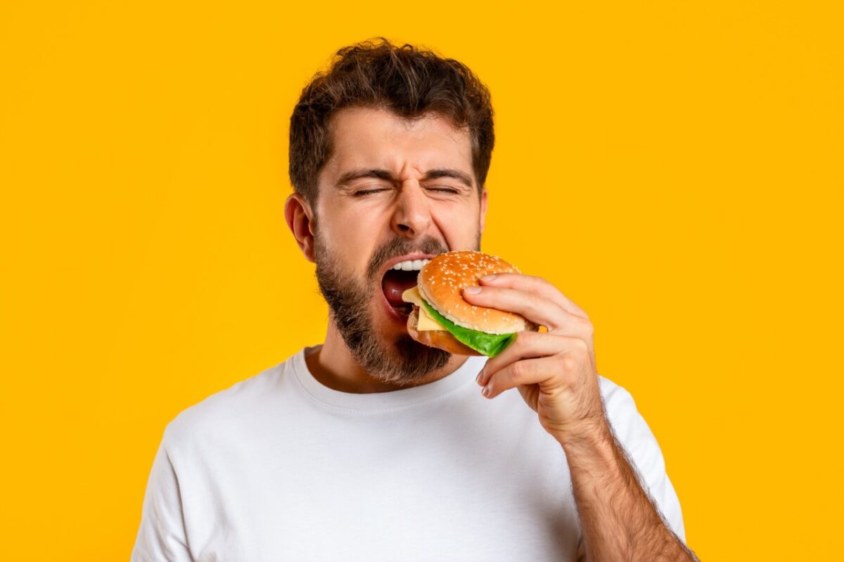 Funny,caucasian,man,takes,bite,of,tempting,burger,on,yellow