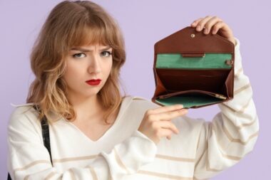 Upset,young,woman,with,empty,wallet,on,lilac,background