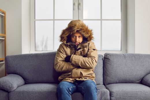 Freezing,man,in,warm,jacket,sitting,on,sofa,at,home.